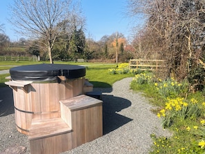 A hot tub with wooden steps, surrounded by a gravel path and yellow flowers. - 1 bedroom accommodation in Southtown, nr Illminster (Southtown, nr Illminster)