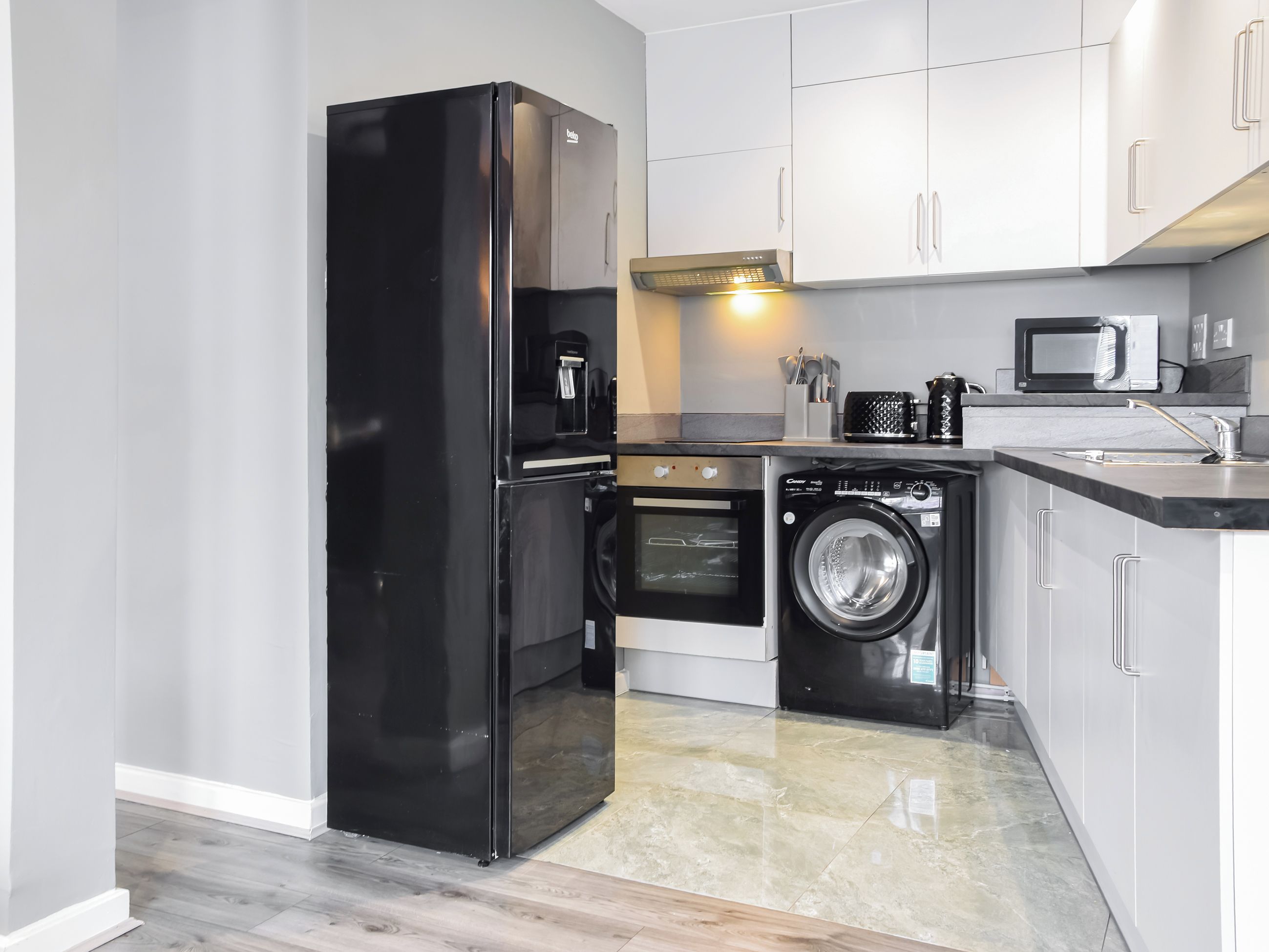 A compact kitchen with a black refrigerator, a built-in oven, a washing machine, and a microwave.