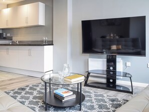 Un soggiorno moderno con un tavolino in vetro, una TV a schermo piatto, un divano e un'area cucina sullo sfondo.