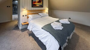 Una cama bien hecha con sábanas blancas, un plaid verde estampado y toallas dobladas con cuidado.