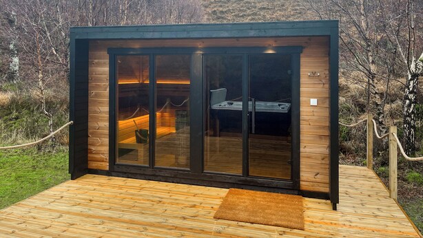 Una cabaña moderna con puerta de vidrio, terraza de madera y un letrero que indica "KOTTHOF SAND".