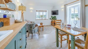 Uma cozinha moderna com bancada de madeira, um espaço de refeições com mesa e cadeiras, uma TV fixada na parede e uma janela com vista.