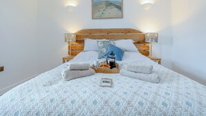 Uma cama com edredom acolchoado, cabeceira de madeira, duas luminárias fixadas na parede e um quadro emoldurado sobre a cama.