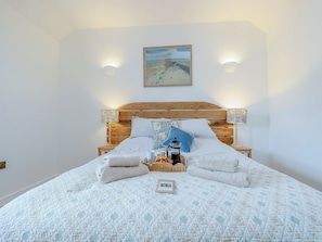 A bed with a quilted bedspread, a wooden headboard, two wall-mounted lamps, and a framed picture above the bed.