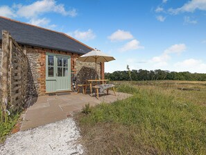 Ein Steinhaus mit einer grünen Tür, einem Steinkamin und einer Terrasse mit Tisch und Stühlen.