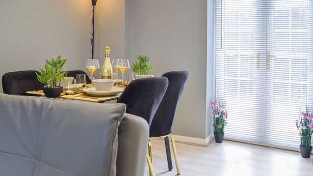 A dining area with a table set for four, a floor lamp, and a window with blinds. - Apartment 3 - UK50137 (Stoke-on-Trent)