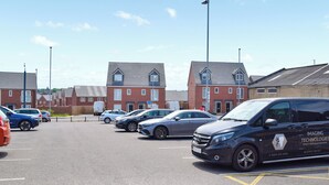 A parking lot with several cars, a building with a red brick facade, and a sign indicating a parking area. - Apartment 3 - UK50137 (Stoke-on-Trent)