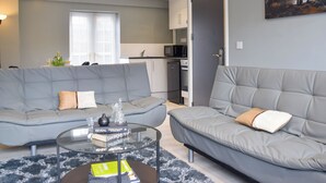 A modern living room with two grey sofas, a glass coffee table, and a kitchen in the background. - Apartment 3 - UK50137 (Stoke-on-Trent)