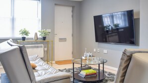 A modern living room with a sofa, a coffee table with books, a TV, and a radiator. - Apartment 3 - UK50137 (Stoke-on-Trent)