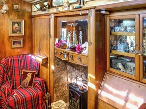 Una habitación acogedora con un sillón de estampado escocés, un aparador de madera con puertas de cristal que exhibe varios objetos, y una chimenea decorada.