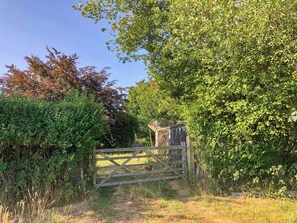 A rustic wooden gate leading into a lush, green area with dense foliage and a clear sky. - 1 bedroom accommodation in Hailsham (Hailsham)