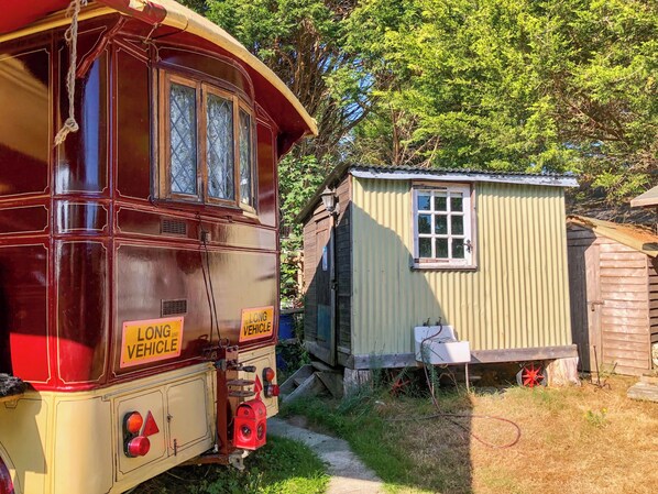 A vintage red bus parked next to a small wooden structure with a corrugated metal roof.