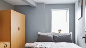A bedroom with a bed, a wardrobe, a window with a view, and a small table with a vase.