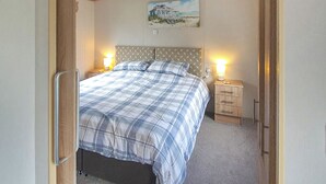 A bedroom with a bed, two bedside tables with lamps, a headboard with a pattern, and a painting on the wall. - 2 bedroom accommodation in Watchet, Somerset (Watchet, Somerset)