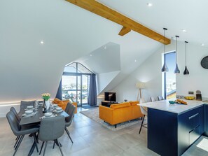 Un loft moderne comprenant un espace repas, une cuisine et un salon, avec un plafond en pente et de grandes fenêtres.