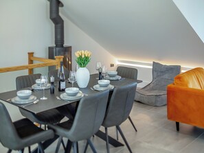 Ein Essbereich mit Tisch für vier Personen, einer Blumenvase und einer Couch im Hintergrund.