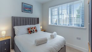 Een net opgemaakt bed met een kussen, een bedlampje en een raam met zonwering.
