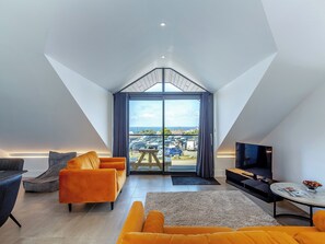 Ein modernes Schlafzimmer im Loft-Stil mit einem großen Dachfenster, einer Sitzecke mit orangefarbenen Sofas und einem Fernseher.