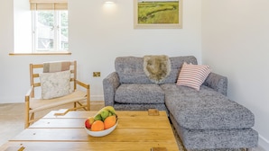 A living room with a sofa, a chair, a wooden coffee table, and a bowl of fruit. - 1 bedroom accommodation in Faversham (Faversham)