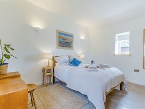 A bedroom with a bed, bedside lamps, a painting, a window, and a plant.