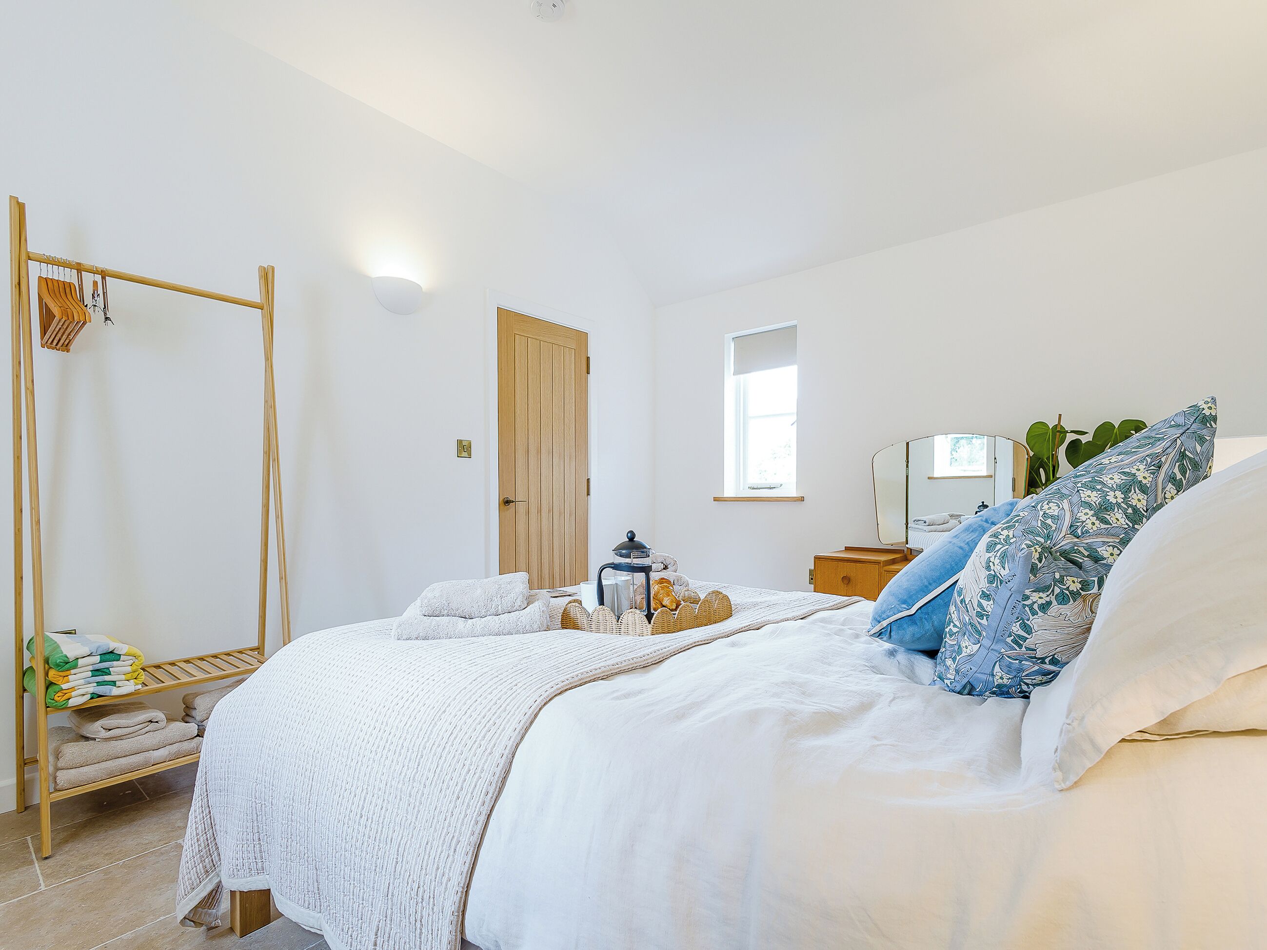 A bedroom with a bed, a wooden wardrobe, a mirror, and a window.
