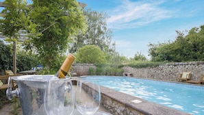 A poolside setting with a stone wall, a wooden table, a metal bucket, and two empty wine glasses. - 1 bedroom accommodation in Faversham (Faversham)