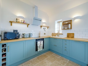 A kitchen with a microwave, toaster, and kettle on the counter, a dishwasher, and cabinets with gold handles.