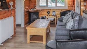 Acogedor interior de cabaña con detalles de madera, un sofá, una mesa, un televisor y una chimenea.