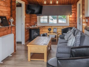 Un intérieur de chalet chaleureux, avec un revêtement mural en bois, un canapé, une table, un téléviseur et une cheminée.