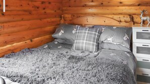 Una habitación tipo cabaña de madera con una cama, ropa de cama gris y un aparador con cajones.