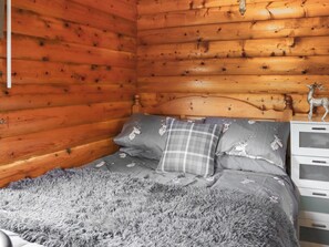 Une chambre rustique en bois, avec un lit, une literie grise et une commode à tiroirs.