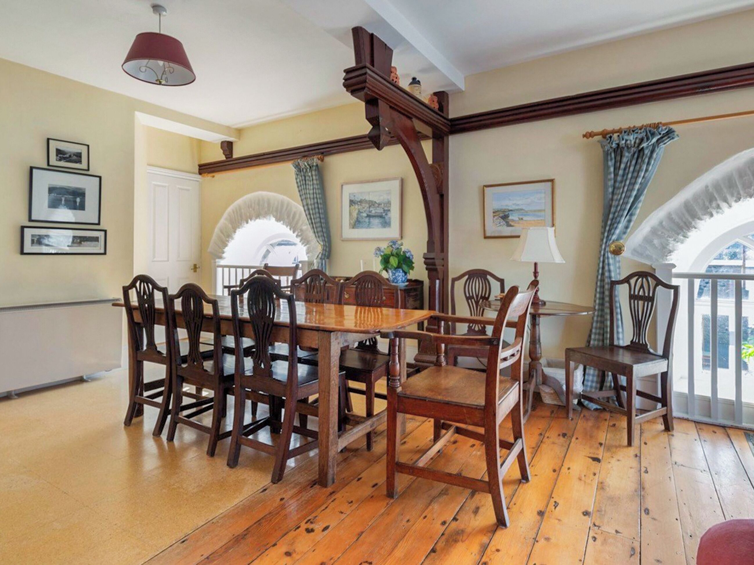 A dining area with a wooden table and chairs, framed pictures on the walls, and a view through an arched window.