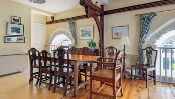 A dining area with a wooden table and chairs, framed pictures on the walls, and a view through an arched window.