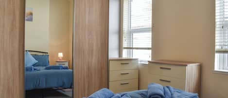 A bedroom with a bed, a dresser, a mirror, and a window with blinds.