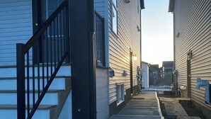 Un étroit sentier mène à un bâtiment portant le numéro « 97 », avec des marches en bois et une rambarde en métal.