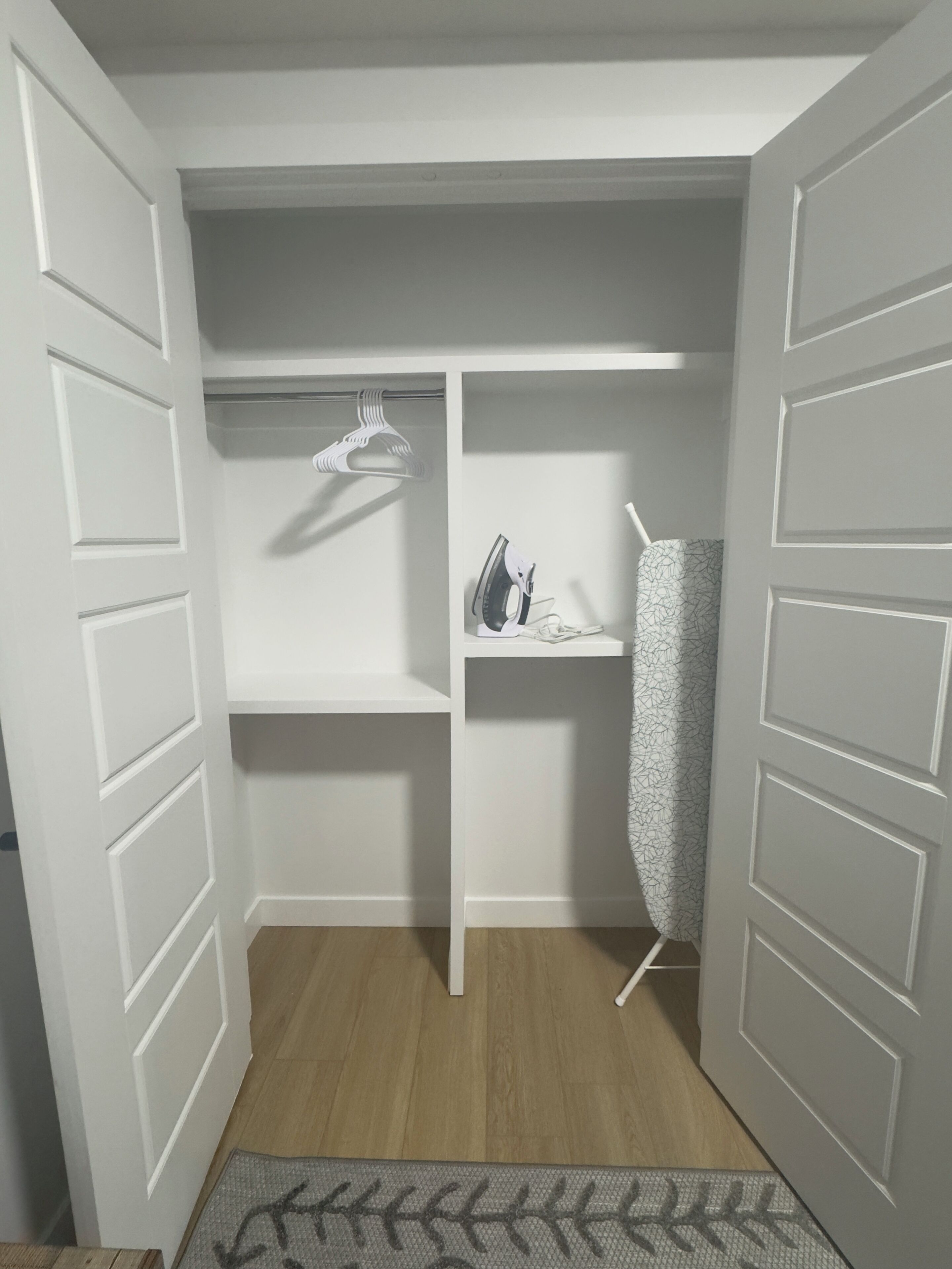 A walk-in closet with white doors, shelves, and a hanging rack.