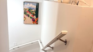 Un escalier avec une rampe, un tableau accroché au mur et une plante sur la plateforme.