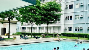 En swimmingpool med folk i vattnet, omgiven av en byggnad med balkonger och träd.