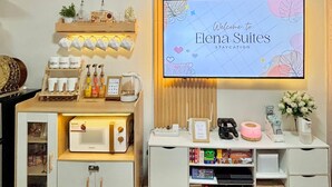 Een kitchenette met een magnetron, koffiezetapparaat en waterkoker. Er is een plank met koffiekopjes en toevoegingen. Een verwelkomingsbord voor Elena Suites hangt aan de muur.