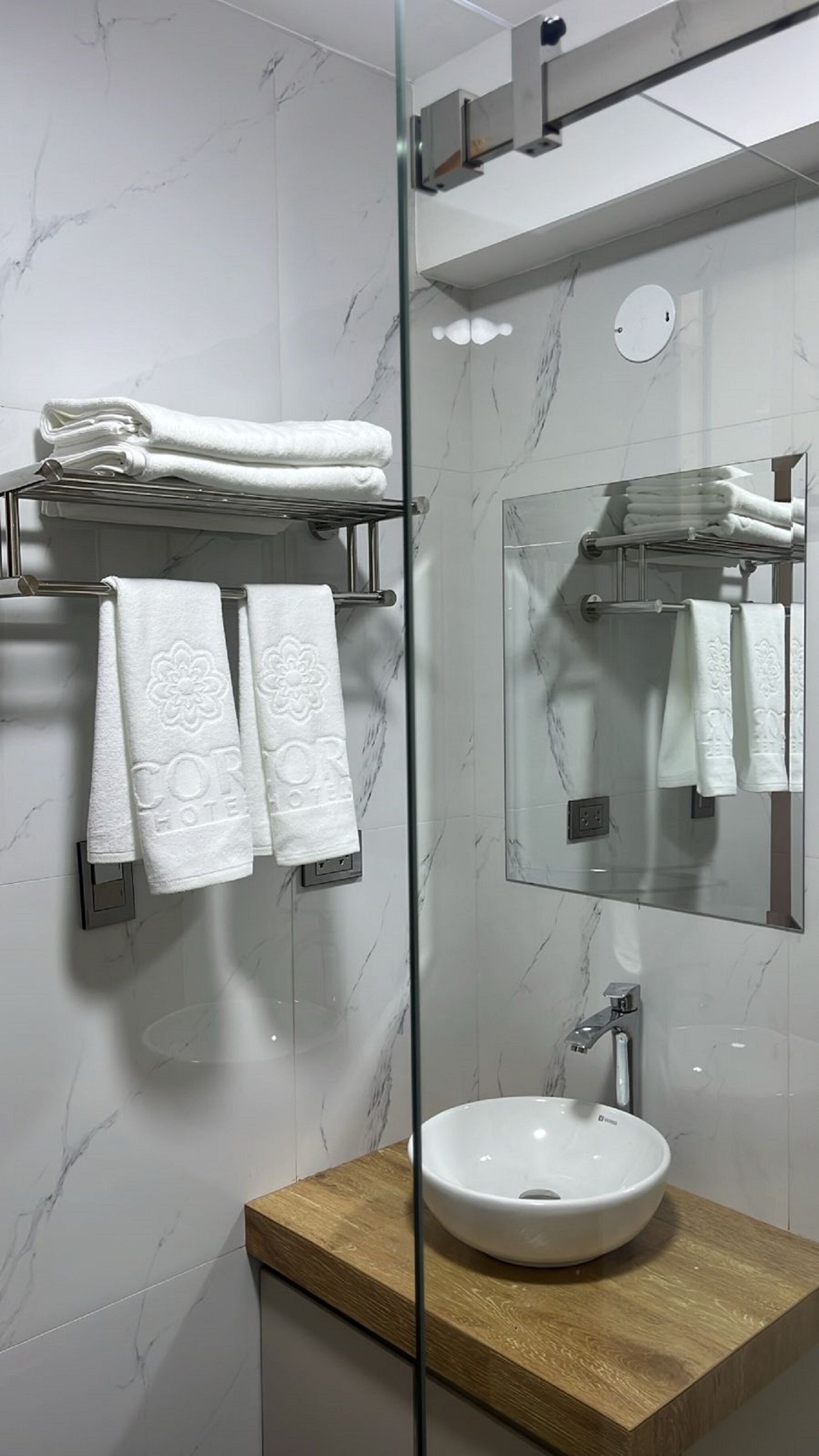 A modern bathroom with a glass shower enclosure, a wooden vanity, and a marble-tiled wall.