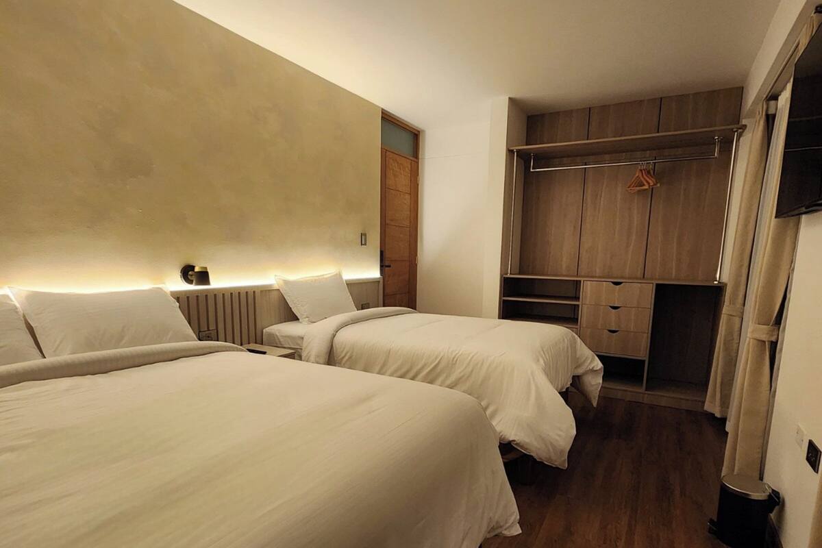 A hotel room with two beds, a wooden wardrobe, and a small kitchenette.