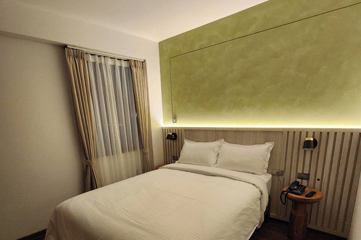 A hotel room with a large bed, a bedside table with a lamp, and a ceiling-mounted light fixture.