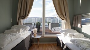 Une chambre avec deux lits, une petite table avec une lampe et une vue sur un balcon agrémenté d’une plante.