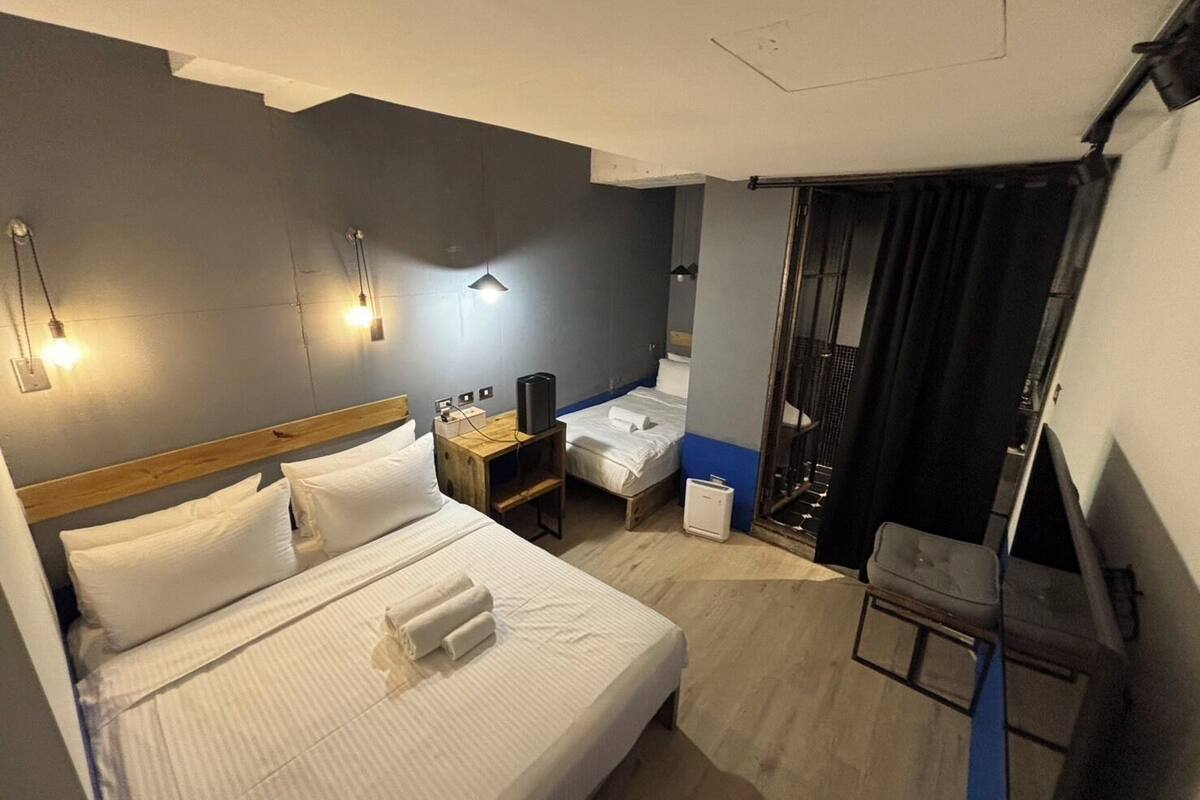 A hotel room with a bed, bedside tables, a desk, a chair, a shower area, and a balcony.