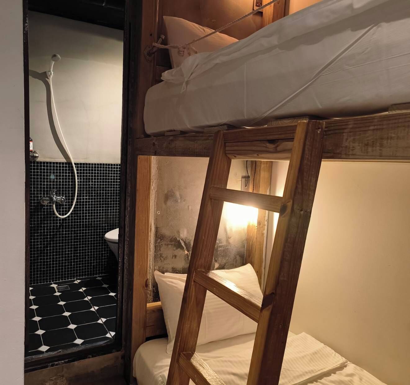 Ein Etagenbett mit Holzlade, eine Dusche mit Schlauch und ein gefliester Boden.