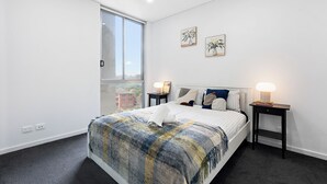 Ein Schlafzimmer mit einem großen Bett, zwei Nachttischen mit Lampen, einem Fenster und zwei gerahmten Bildern an der Wand.