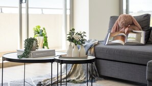 Ein modernes Wohnzimmer mit einem grauen Sofa, einem kleinen runden Tisch mit Buch und Vasen sowie einem großen Fenster mit Blick auf die Stadt.
