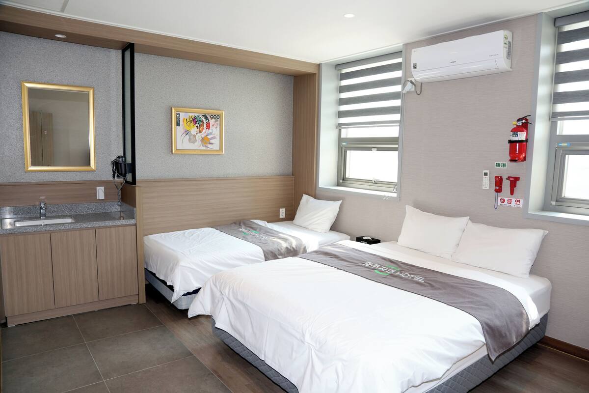 Een hotelkamer met twee bedden, een wastafel en een raam met jaloezieën.