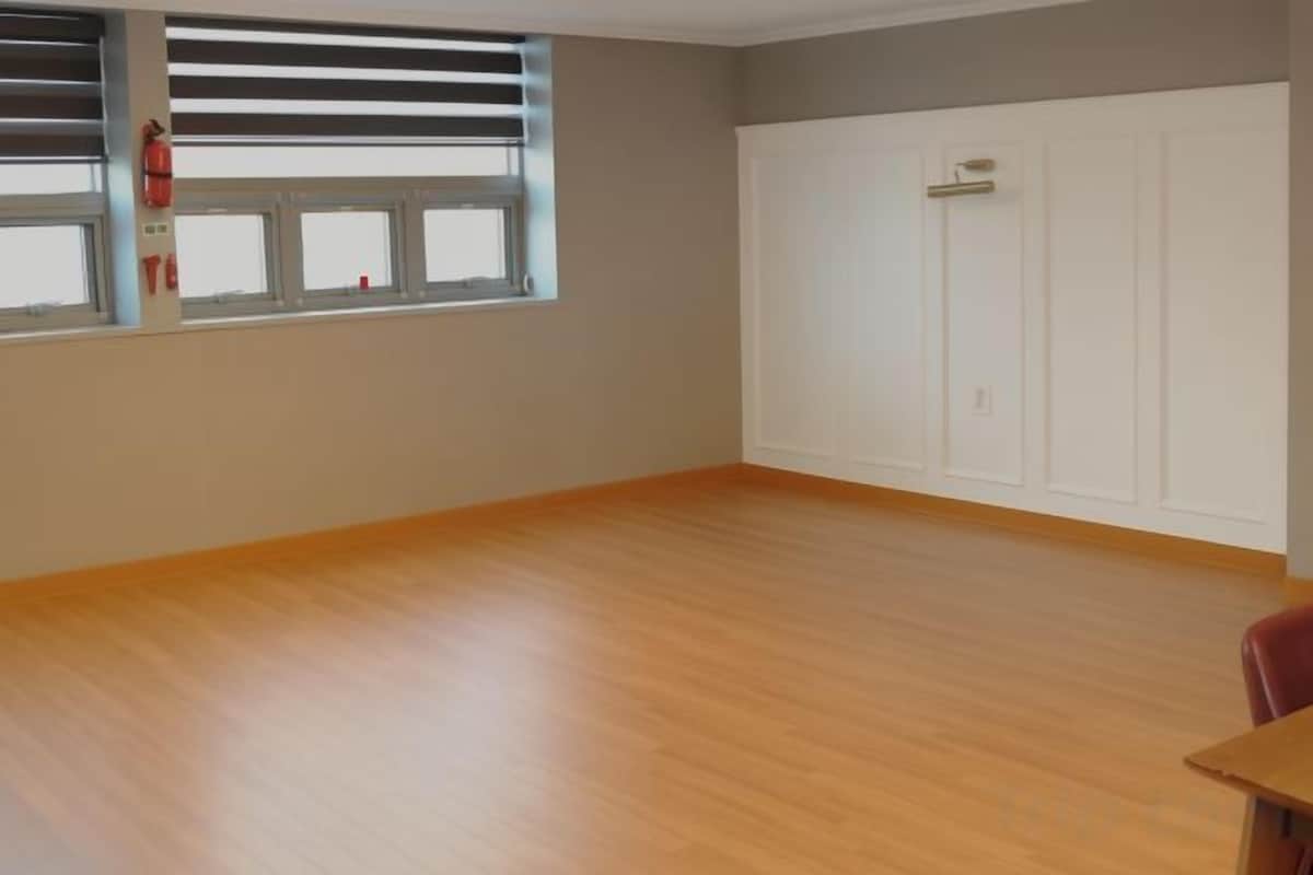 Une pièce avec un plancher en bois, une fenêtre avec des stores, une porte blanche et une chaise rouge.
