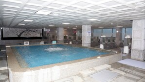 Μια μεγάλη εσωτερική πισίνα με πλακάκια στο δάπεδο και ένα ταβάνι με σχέδιο σε μορφή πλέγματος.